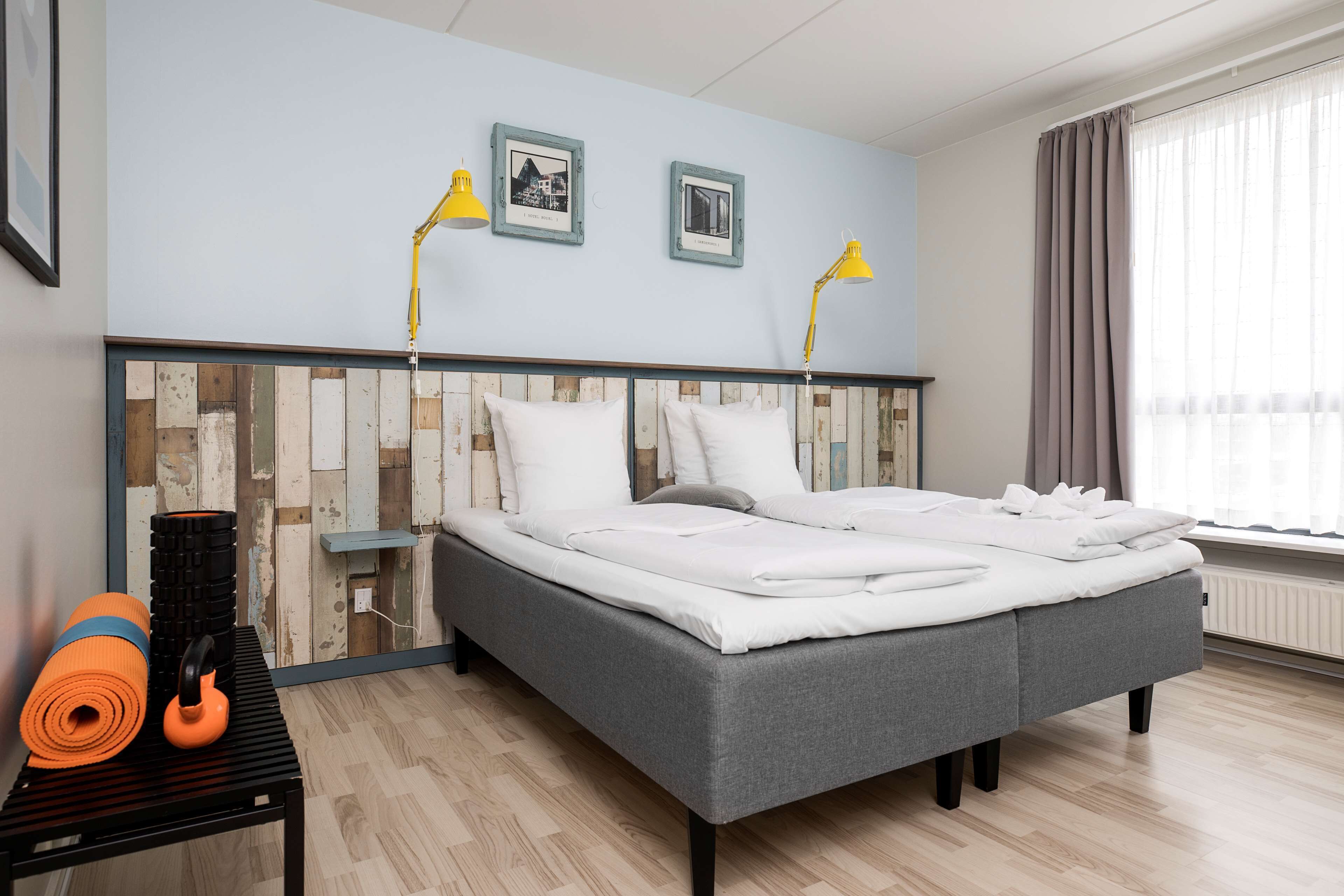 A neatly made bed with white linens, a grey headboard, and two framed pictures on the wall.