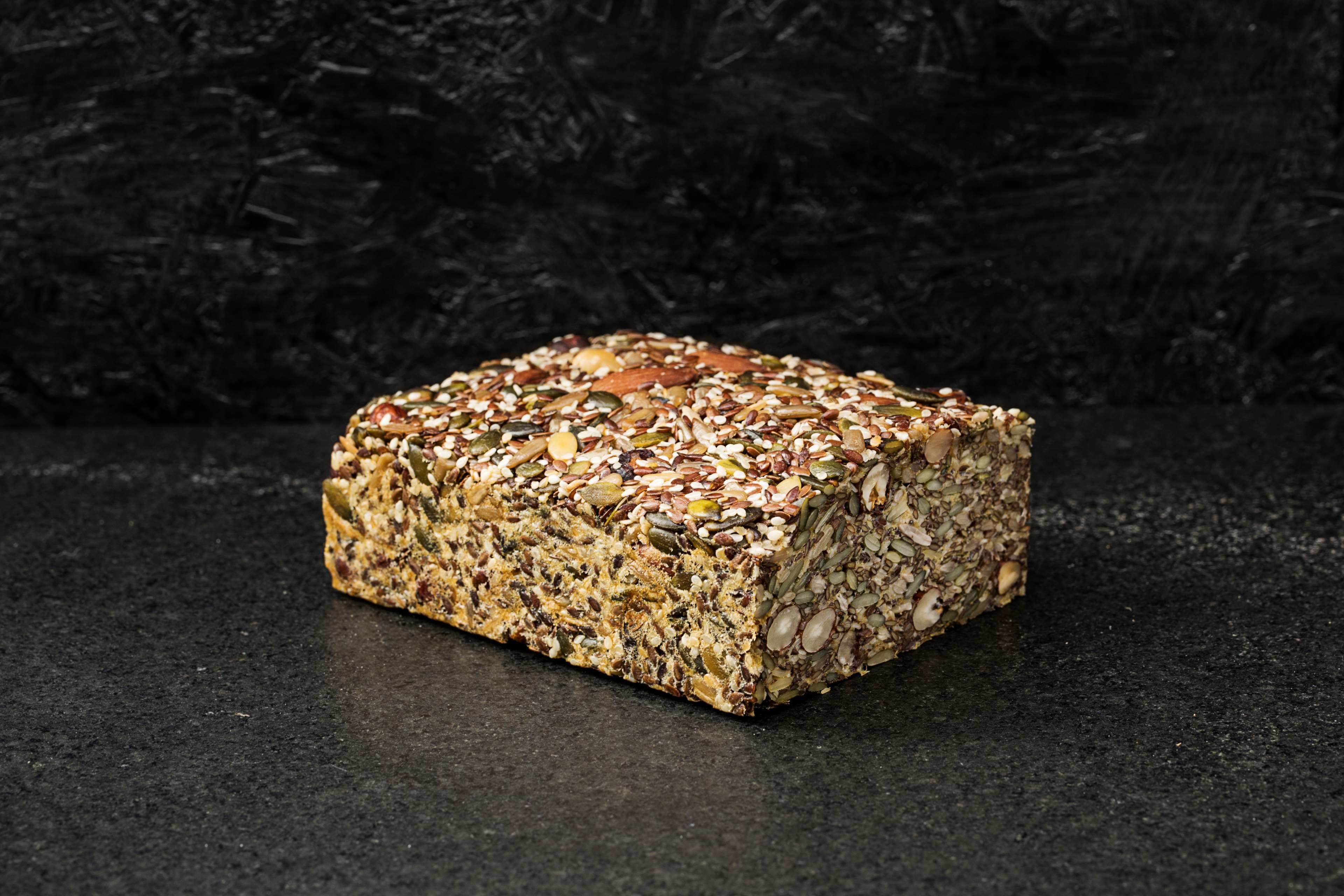 A loaf of mixed grain bread on a dark surface.