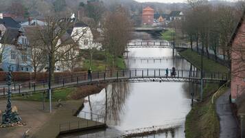 Un paseo junto al río con un puente, una estatua y casas al fondo.