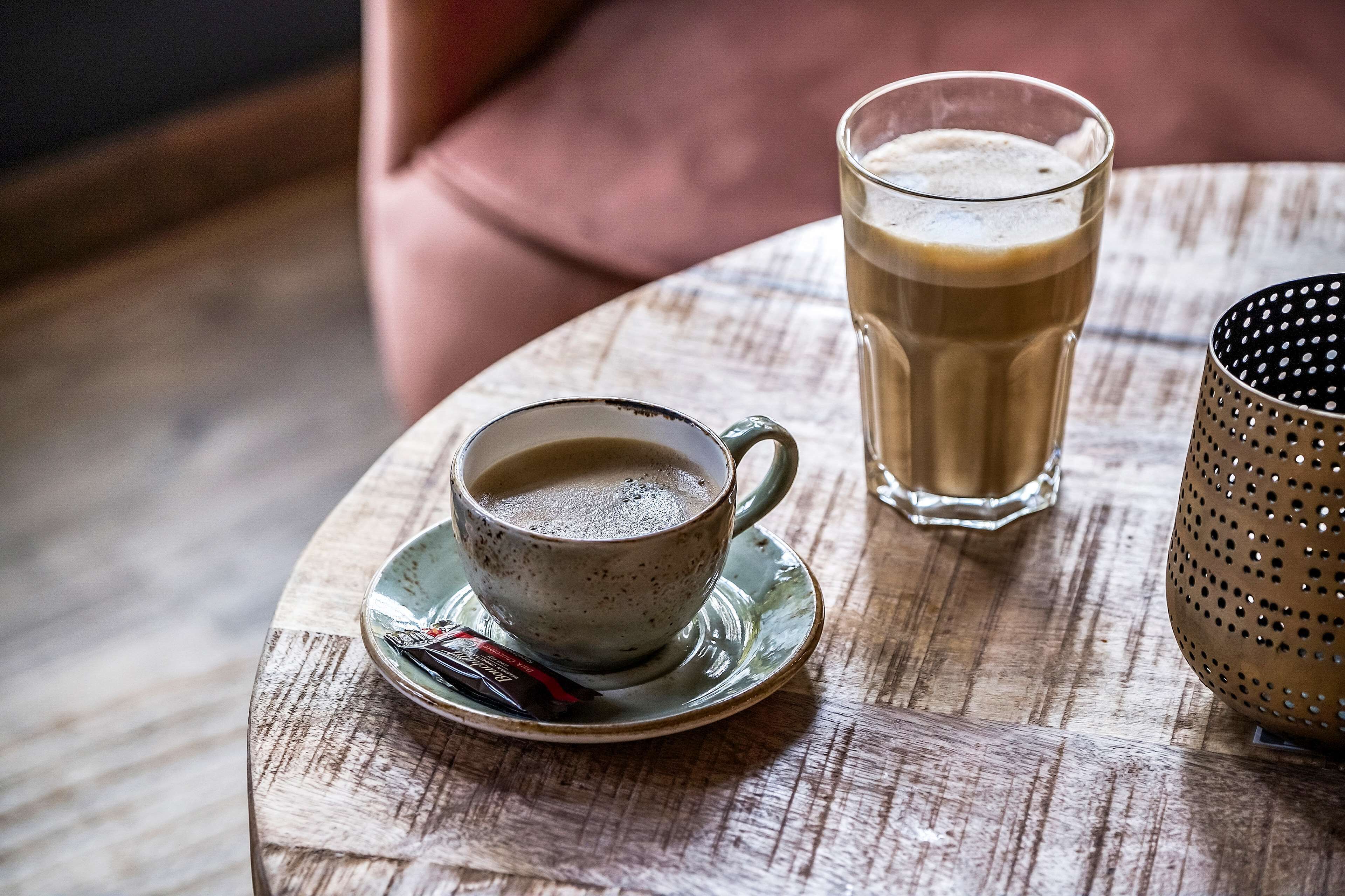 Una mesa de madera redonda con una taza de café y un vaso de café helado encima.