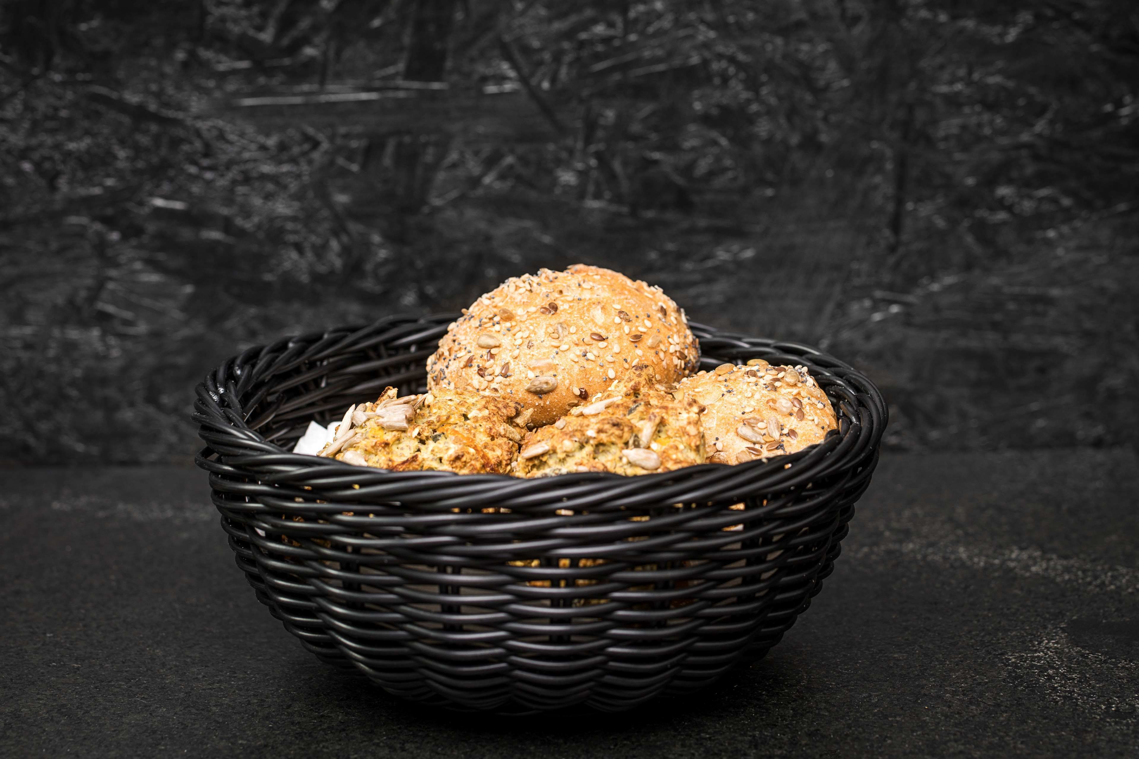 A black woven basket containing several round, multi-grain bread rolls.
