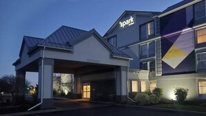 A hotel entrance with a covered parking area, a bike parking symbol, and a large building with a 'spark' sign. - Spark by Hilton Rochester University Area (Rochester)