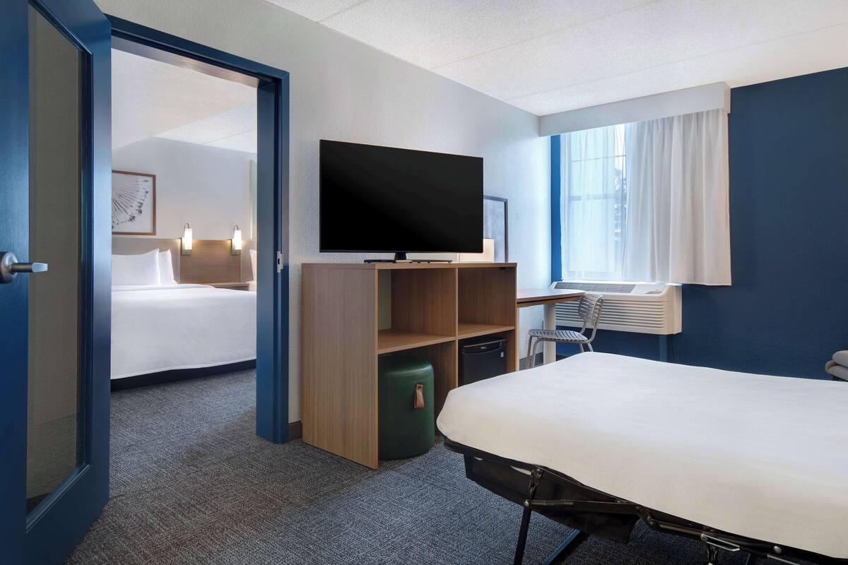 A hotel room with a bed, a television, a desk, and a window with curtains.