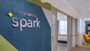 A modern interior with a sign reading "It only takes a spark" and a glass door leading to a room with a yellow chair and a vending machine. - Spark by Hilton Rochester University Area (Rochester)