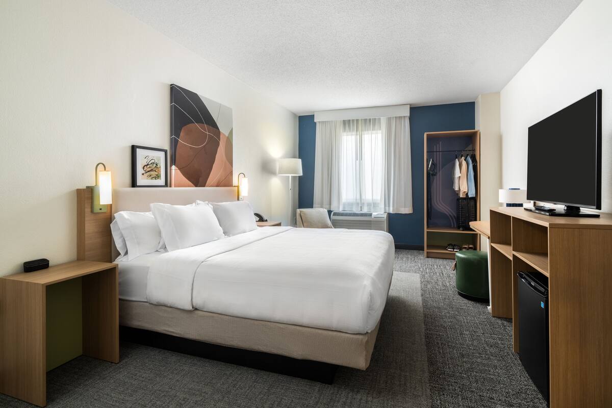 A hotel room with a large bed, a desk with a television, a wardrobe, and a window with curtains.