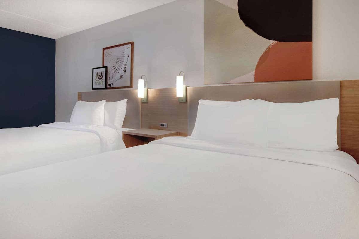 A hotel room with two beds, a nightstand, wall-mounted reading lights, and artwork on the wall.