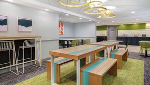 A modern dining area with wooden tables and benches, green chairs, and a bar area with stools. - Spark by Hilton Rochester University Area (Rochester)