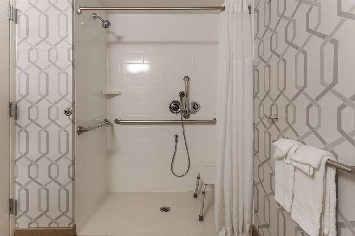 A walk-in shower with a glass door, a handrail, a showerhead, and a towel rack.