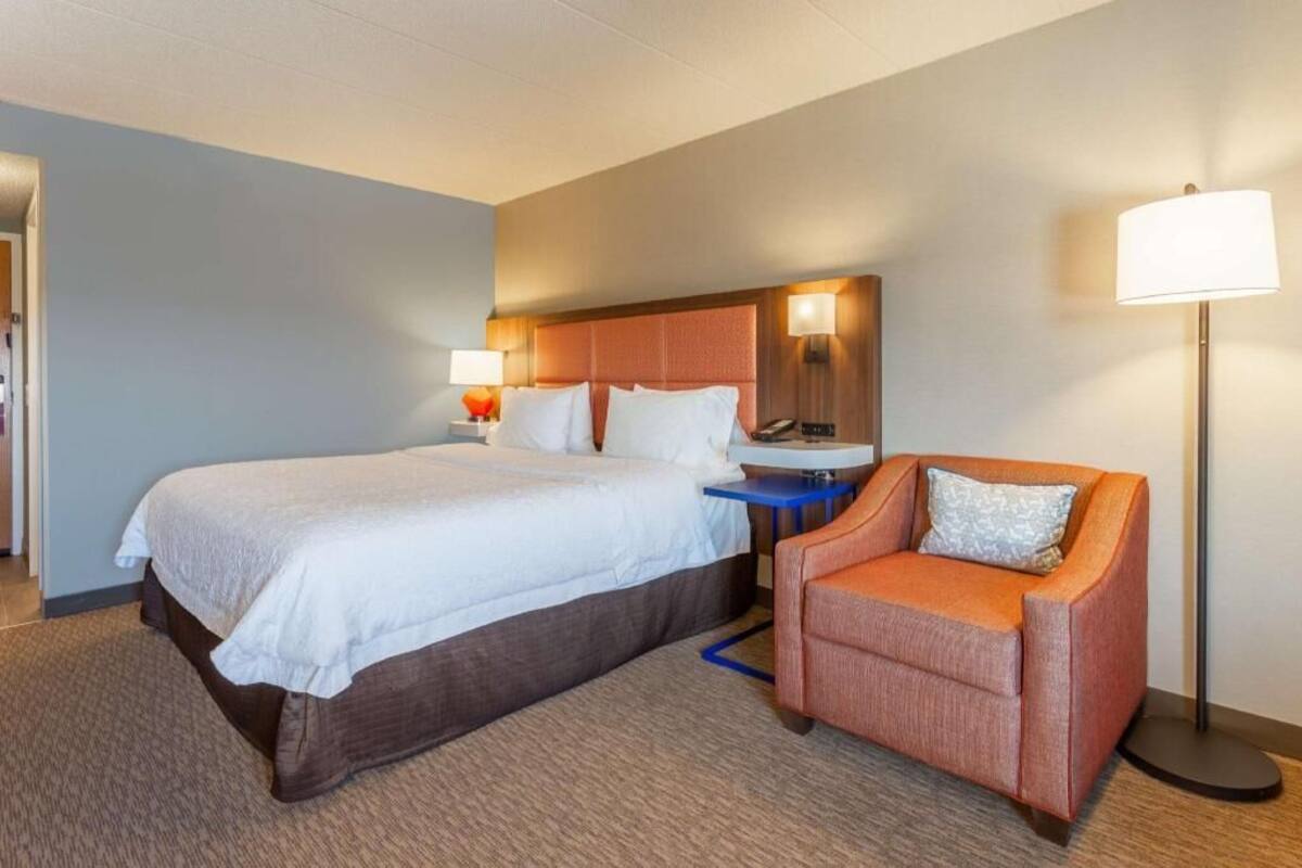 A hotel room with a large bed, a chair, a desk, and a lamp.