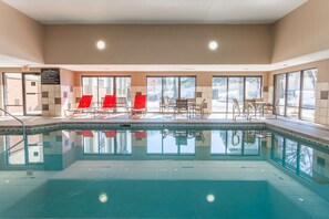 An indoor swimming pool with clear glass walls, red chairs, and a table with chairs. - Hampton Inn Madison East Towne Mall Area (Madison)