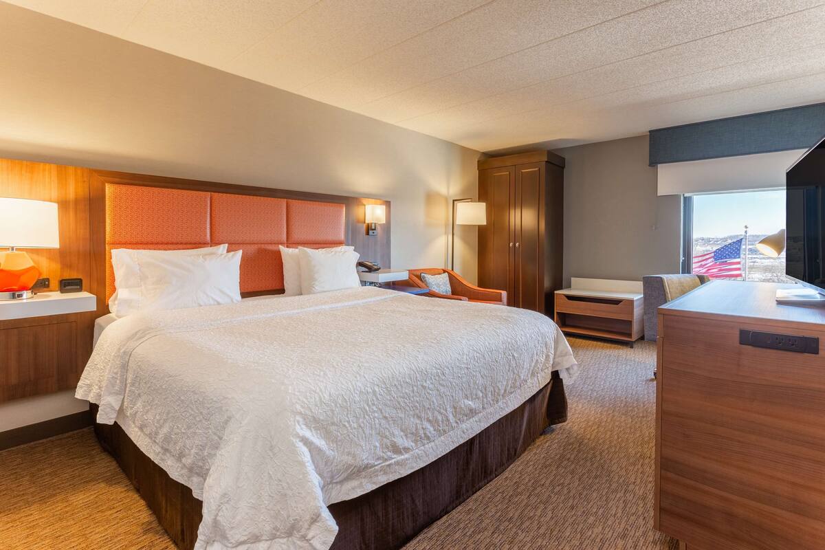 A hotel room with a large bed, a desk, a chair, and a wardrobe.