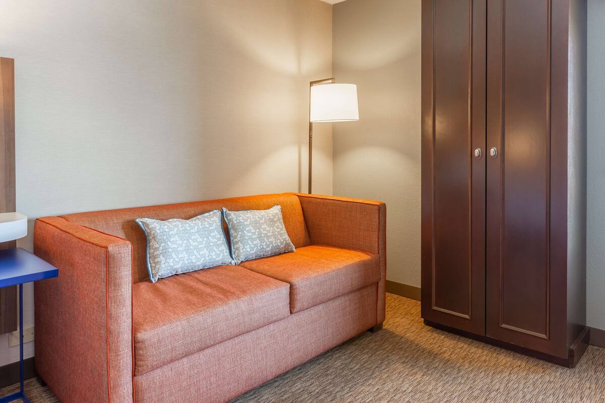 A hotel room with a sofa, a lamp, and a wardrobe.
