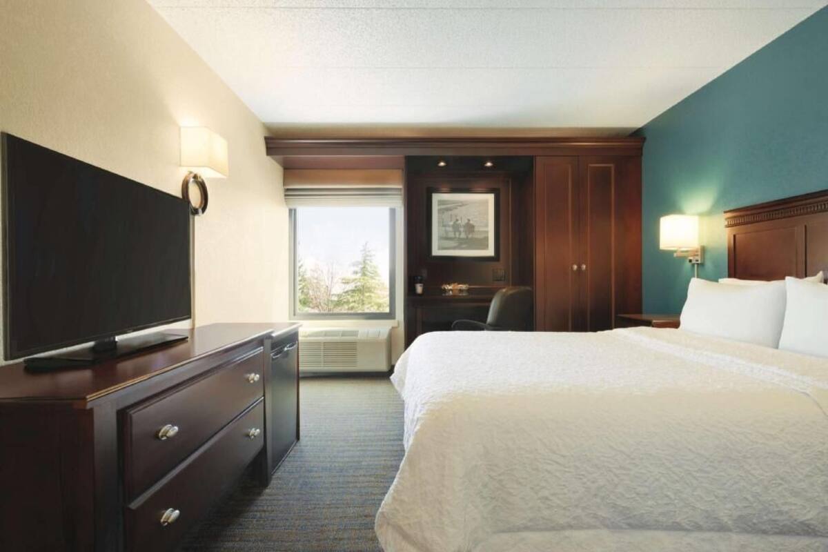A hotel room with a bed, a television on a dresser, a desk, and a window.