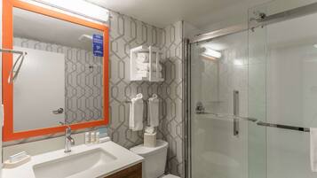 A modern bathroom with a glass shower enclosure, a white sink with a wooden vanity, and a mirror with an orange frame.