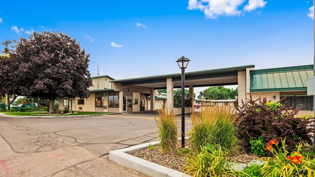 A hotel with a covered parking area, a large tree, and a well-maintained garden with various plants and flowers. - Best Western Paradise Inn & Resort (Fillmore)
