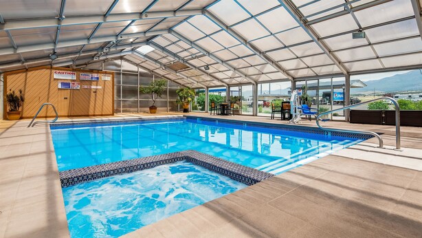 An indoor swimming pool with a glass ceiling, surrounded by lounge chairs and potted plants. - Best Western Paradise Inn & Resort (Fillmore)