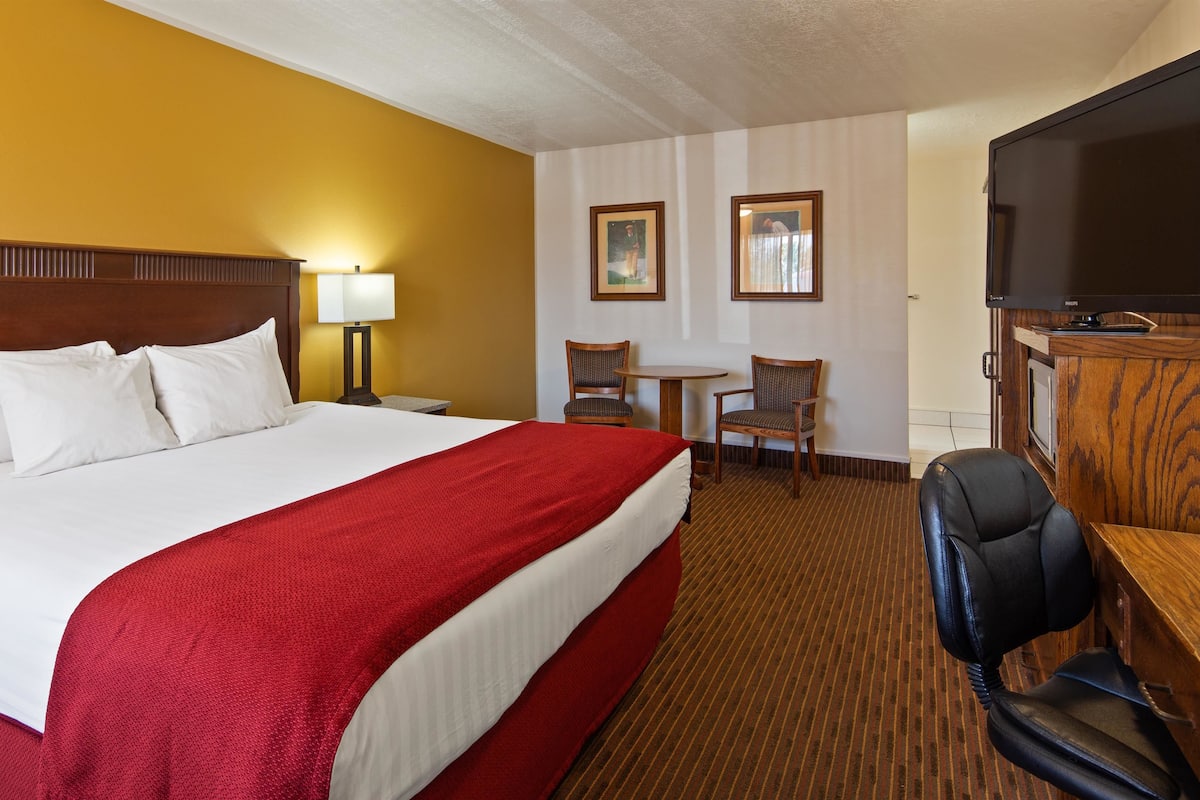 A hotel room with a large bed, a television, a desk with two chairs, and a wooden cabinet.