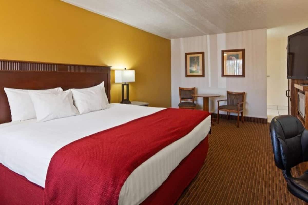 A hotel room with a large bed, a desk with a chair, a television, and two framed pictures on the wall.