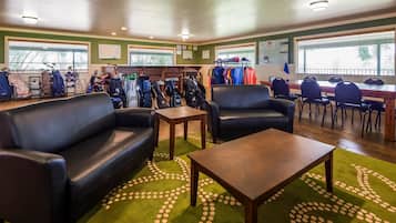 A room with two black leather sofas, a wooden coffee table, and a green carpet with a white pattern. There are golf bags and clothing racks in the background.