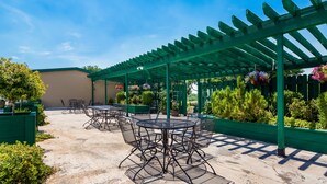 An outdoor patio with green pergola, tables, and chairs, surrounded by greenery and plants. - Best Western Paradise Inn & Resort (Fillmore)