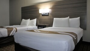 A hotel room with two beds, a nightstand, and a wall-mounted lamp.