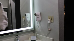 A bathroom with a large mirror, two hair dryers mounted on the wall, and a sink with a faucet.