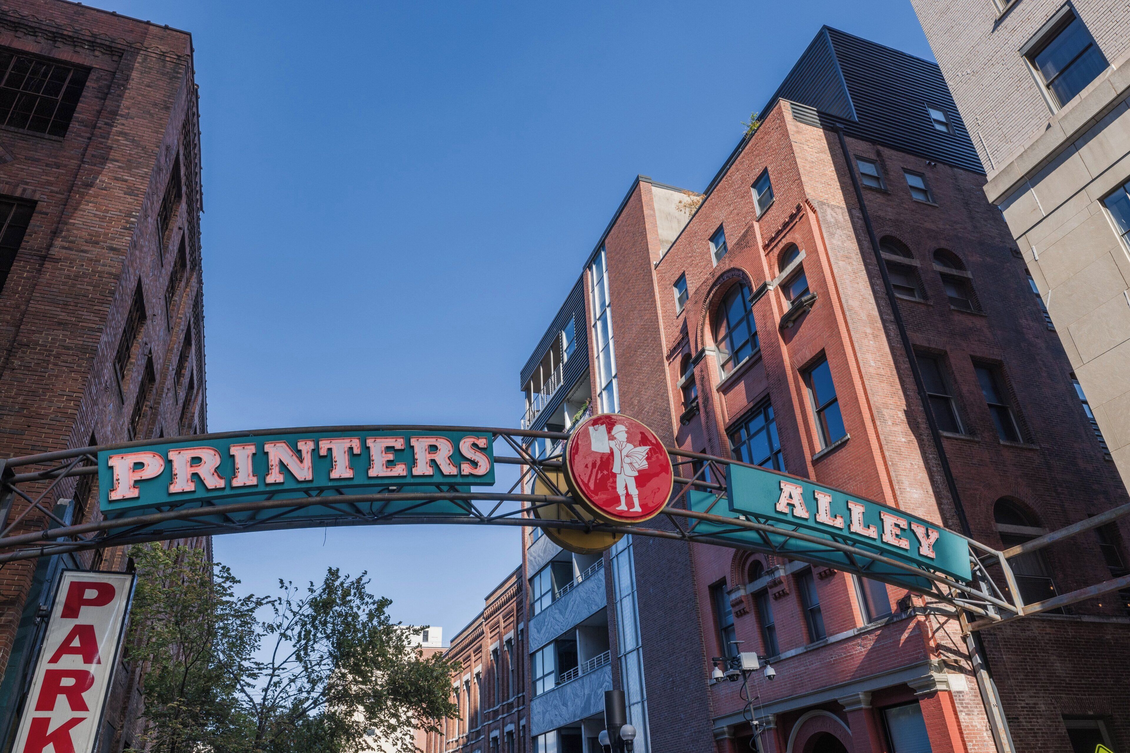 Una señal de calle para Printers Alley con un semáforo de parada y una señal de parque.