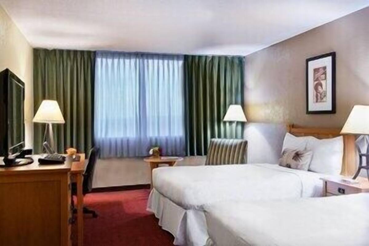 Ein Hotelzimmer mit zwei Betten, einem Schreibtisch, einem Stuhl, einem Fernseher und einem Fenster mit Vorhängen.