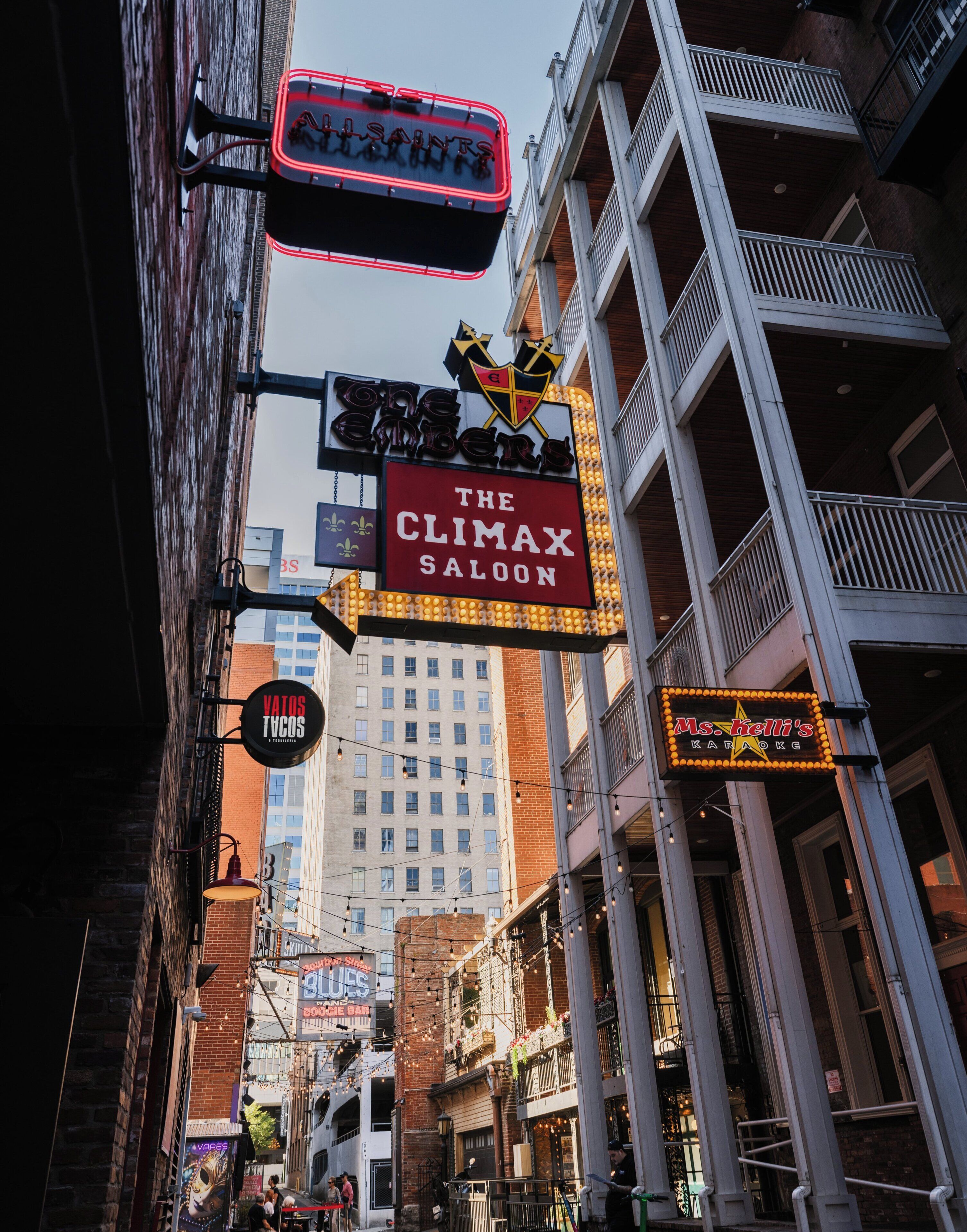 A street view with various illuminated signs, including 'The Climax Saloon' and 'Vatos Tacos.'