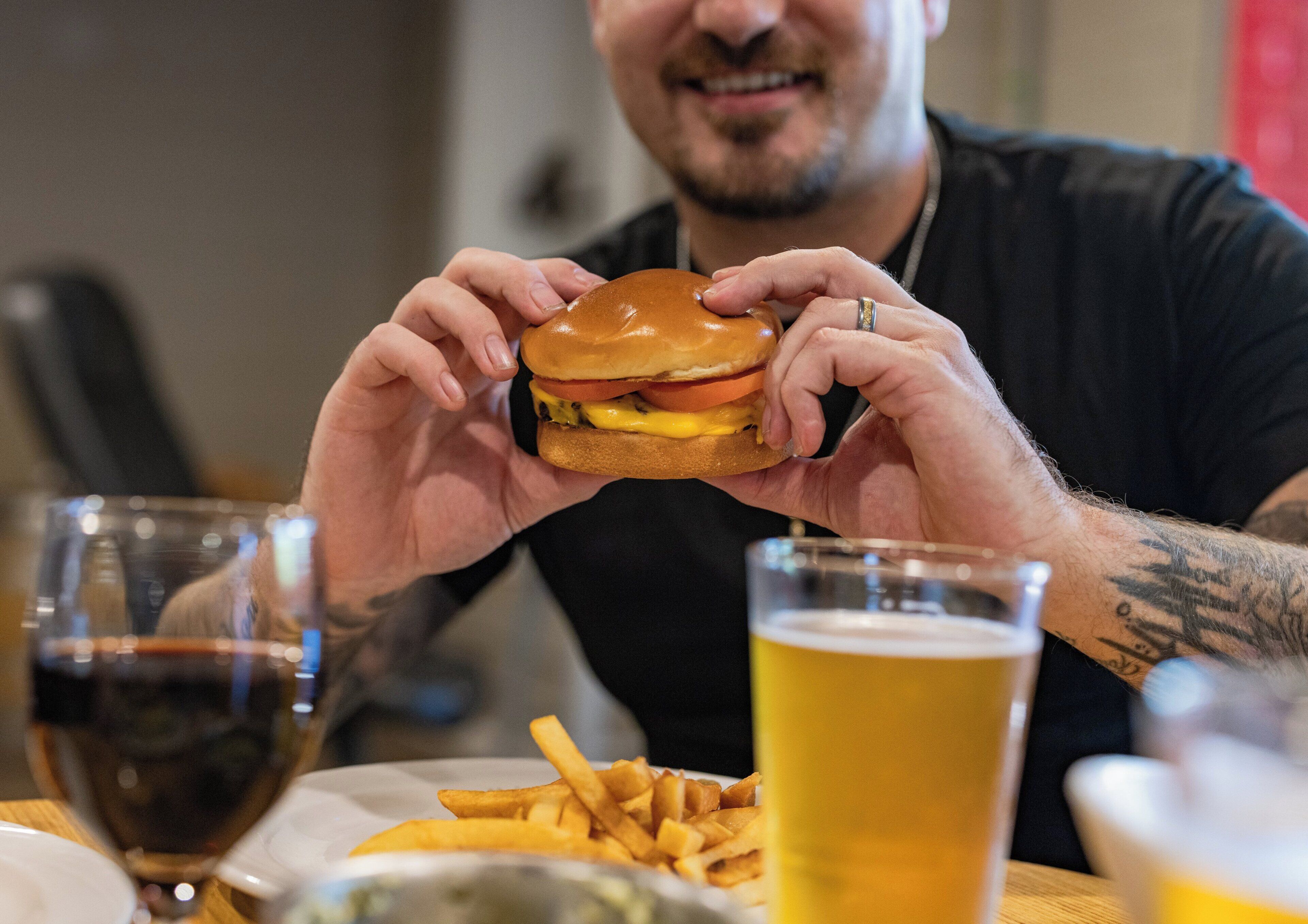 Une personne tenant un hamburger, un verre de bière et une assiette de frites.