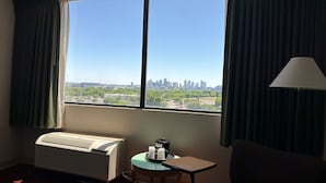 A hotel room with a large window, an air conditioning unit, a table with a lamp, and a view of a city skyline. - Millennium Hotel Maxwell House Nashville (Nashville)