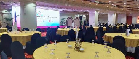 A conference room with round tables, black chairs, and a stage with a presentation screen.