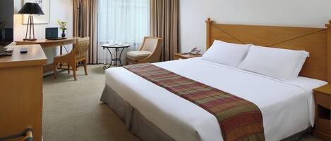 A hotel room with a large bed, a desk with a computer, a chair, a TV, and a lamp.