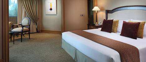 A hotel room with a large bed, a chair, a desk, and a window with curtains.