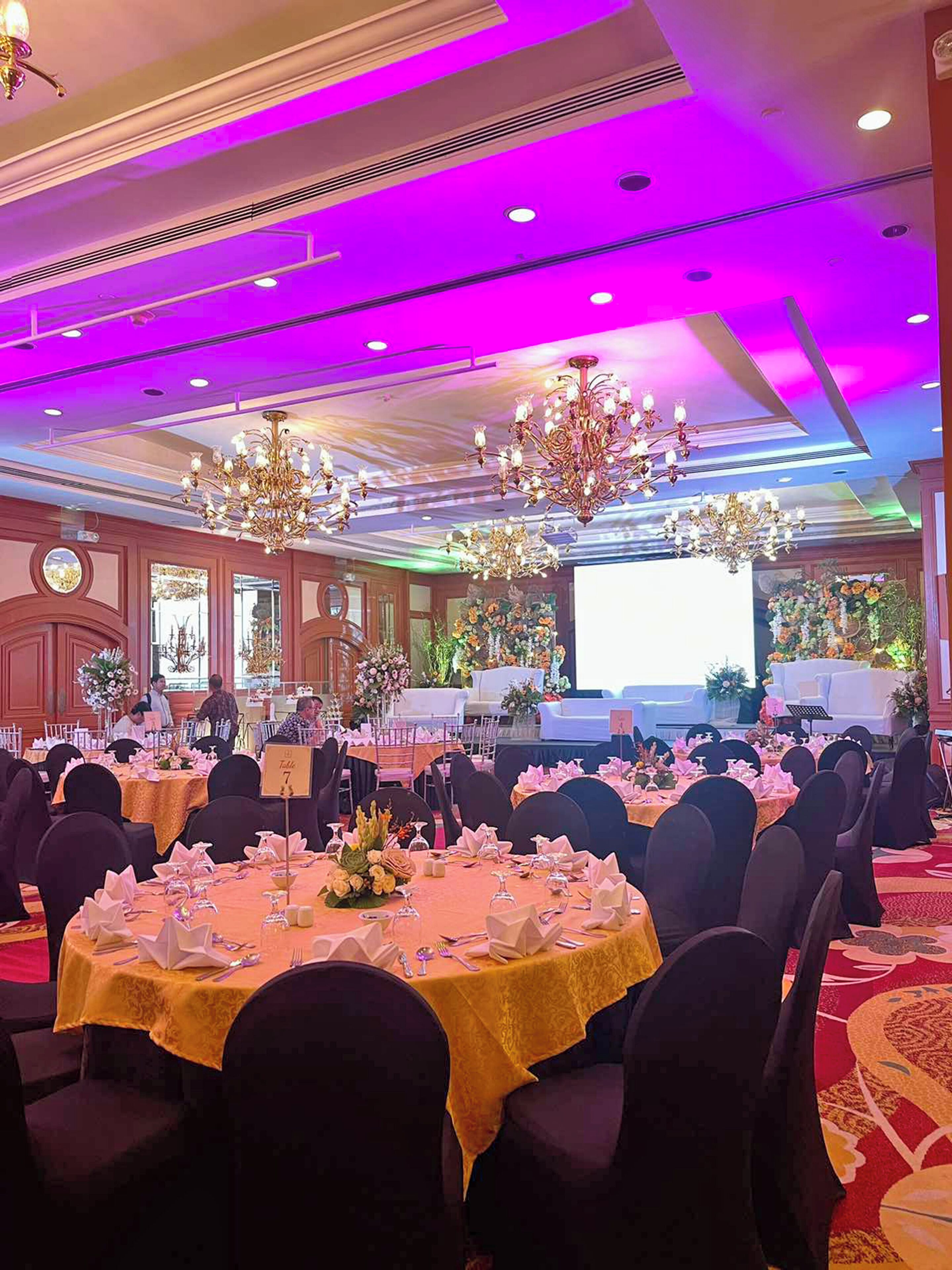 A banquet hall with round tables, dark chairs, and chandeliers.