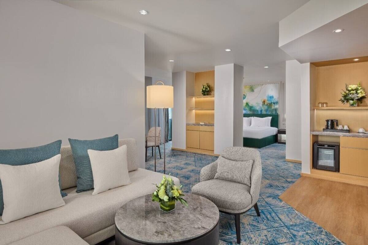 A modern hotel room with a sofa, armchair, and a coffee table with a vase of flowers.