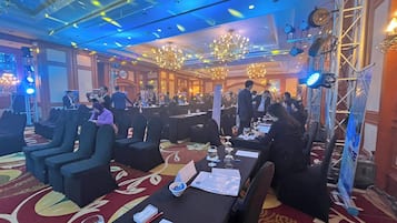 A banquet hall with round tables, black chairs, and chandeliers.