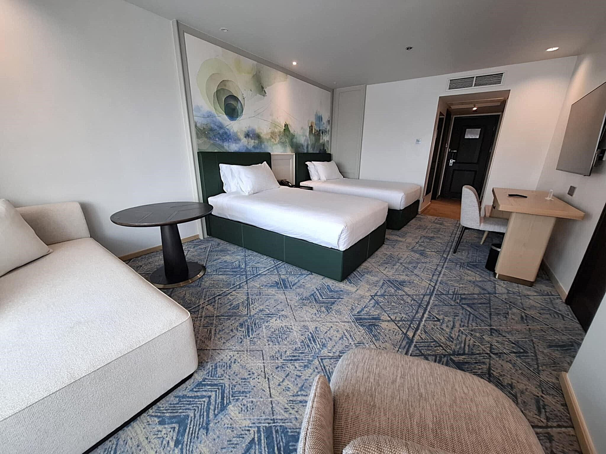 A hotel room with two beds, a sofa, a small table, and a TV.