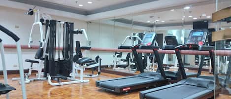 Ett gym med löpband, styrketräningsmaskiner och en vägg täckt med speglar.