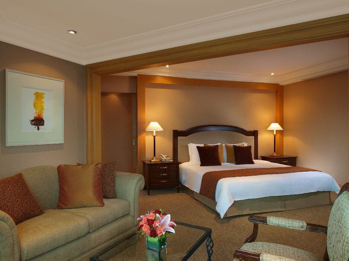 A hotel room with a large bed, two bedside tables with lamps, a sofa, and a small table with flowers.