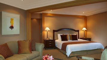 A hotel room with a large bed, two bedside tables with lamps, a sofa, and a small table with flowers.
