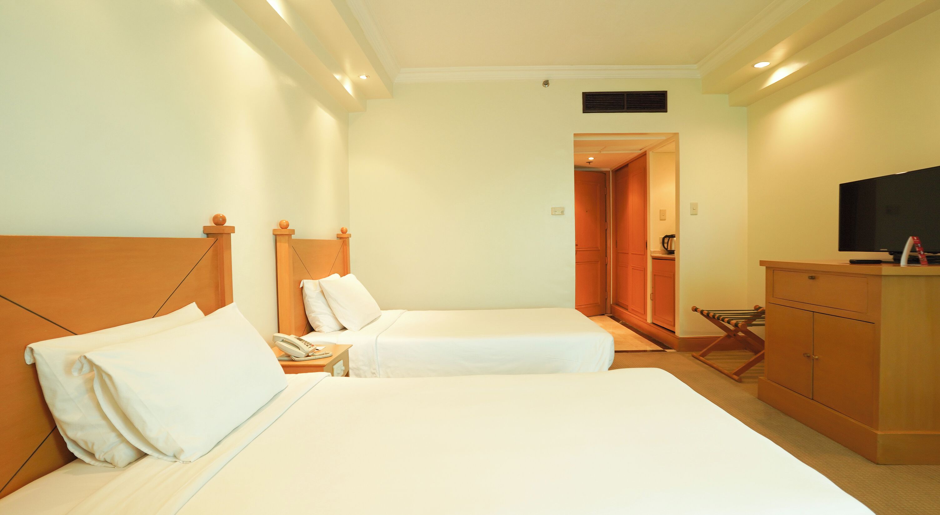 Habitación de hotel con dos camas, un televisor, un escritorio con teléfono y un armario.
