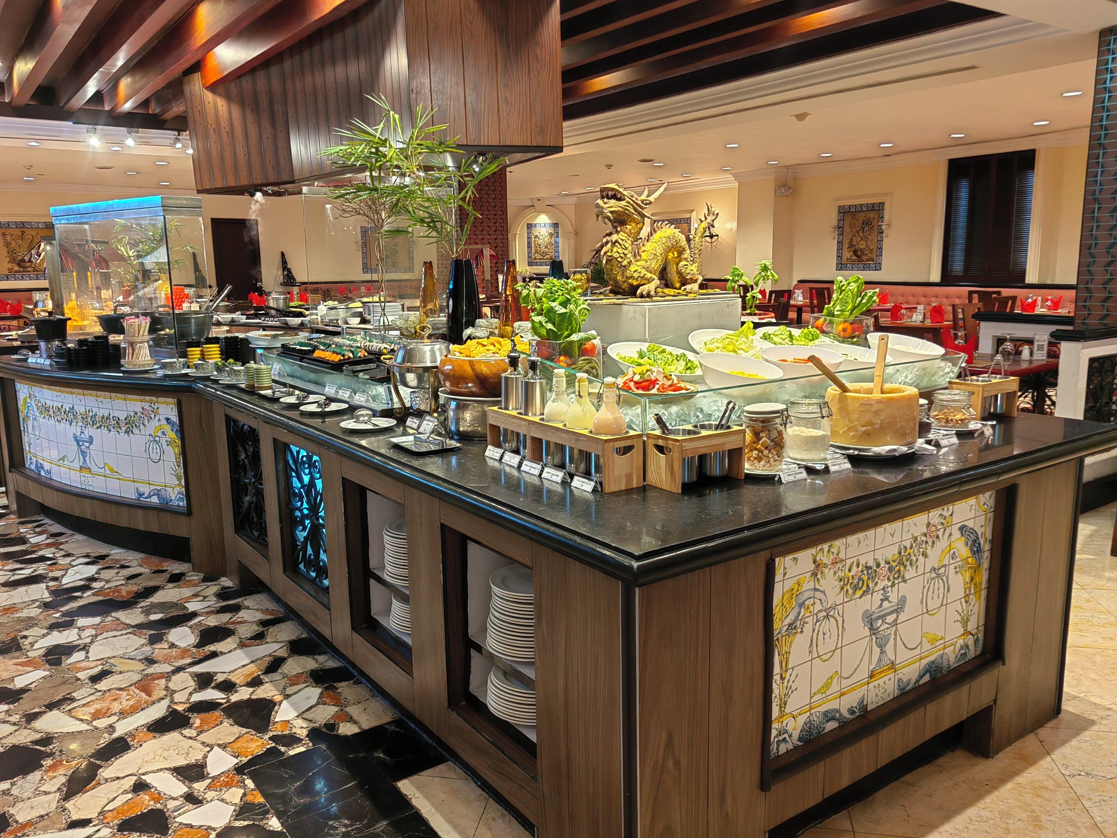 A buffet area with a variety of food options, a decorative golden dragon statue, and a tiled floor with a geometric pattern.
