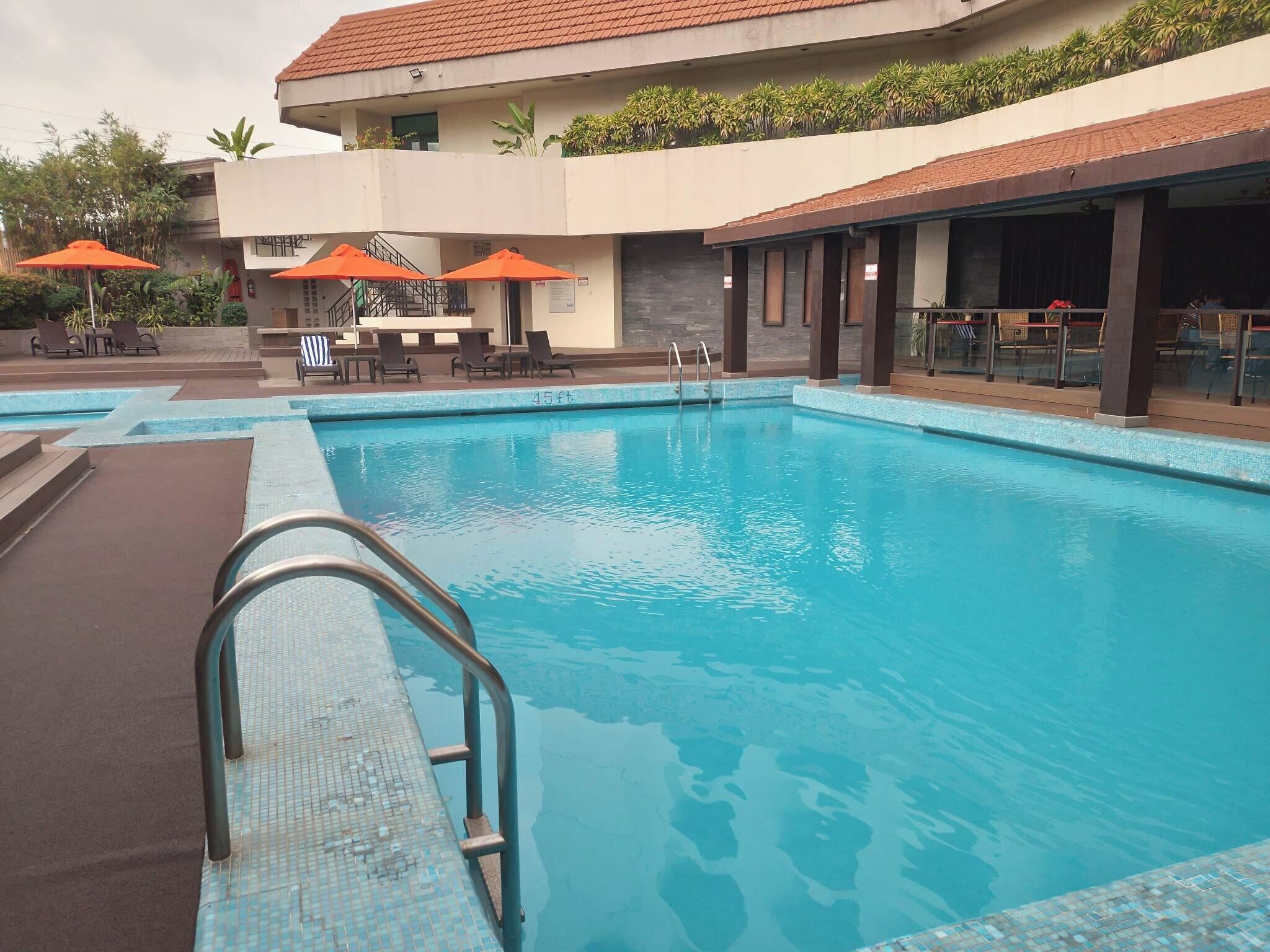 Una piscina con borde de azulejos, sillas de descanso y sombrillas naranjas.