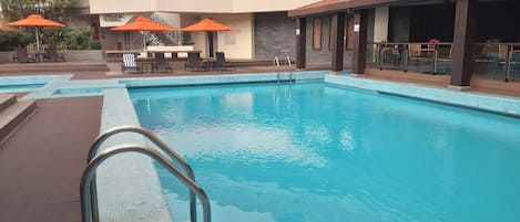 Una piscina con borde de azulejos, sillas de descanso y sombrillas naranjas.