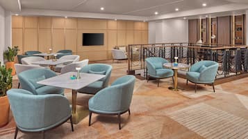 Un hall d’hôtel moderne, doté d’espaces aménagés avec des sièges, d’un téléviseur fixé au mur et d’une rambarde décorative.