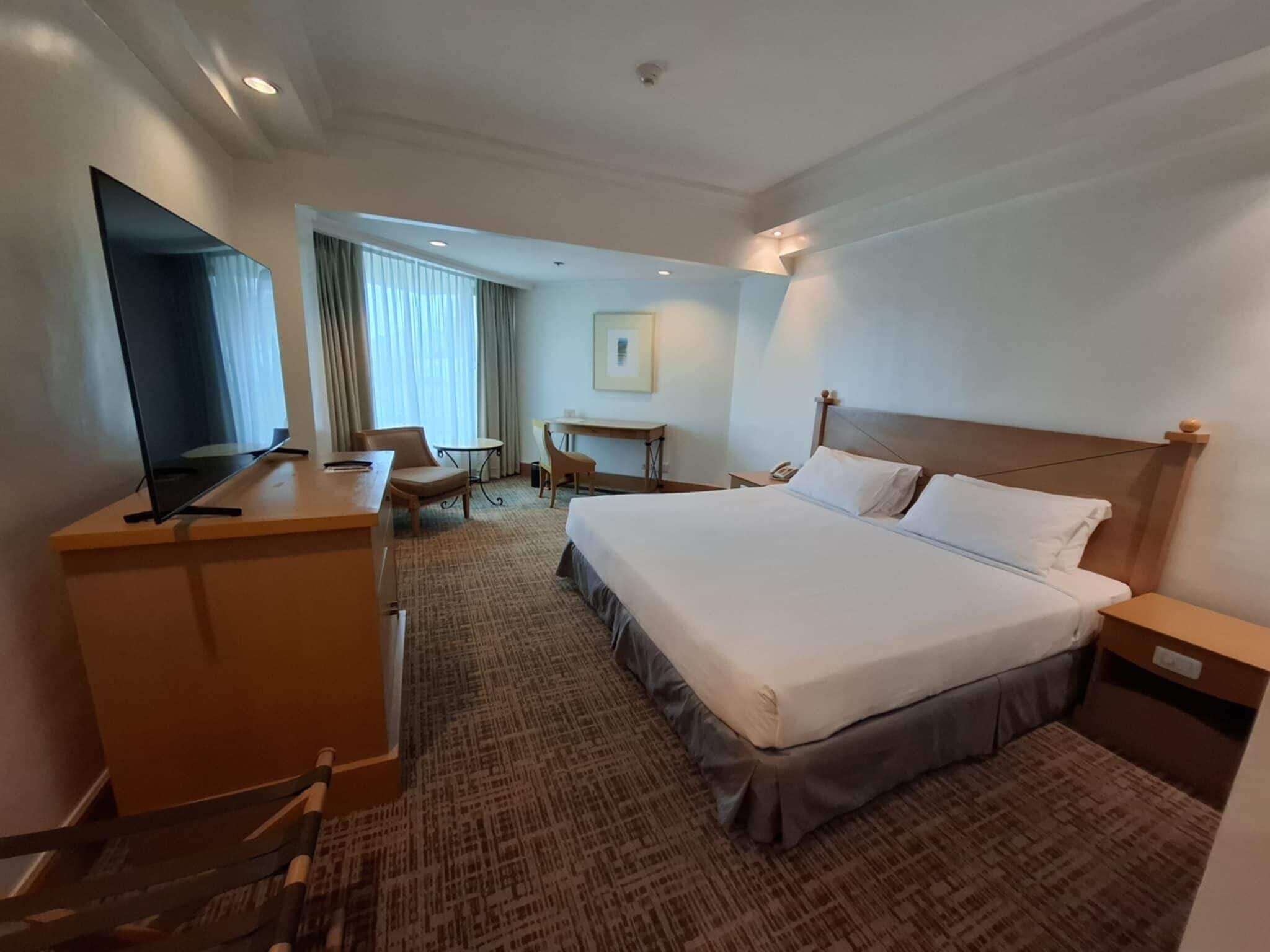 Une chambre d’hôtel avec un lit, un bureau, une chaise, une télévision et une fenêtre avec des rideaux.