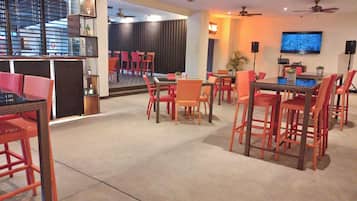 Ein großzügiger Innenbereich mit verschiedenen Sitzgelegenheiten, darunter eine Bar mit Theke und Stühlen sowie ein Essbereich mit Tischen und Stühlen. Deckenventilatoren und ein an der Wand montierter Fernseher sind vorhanden.