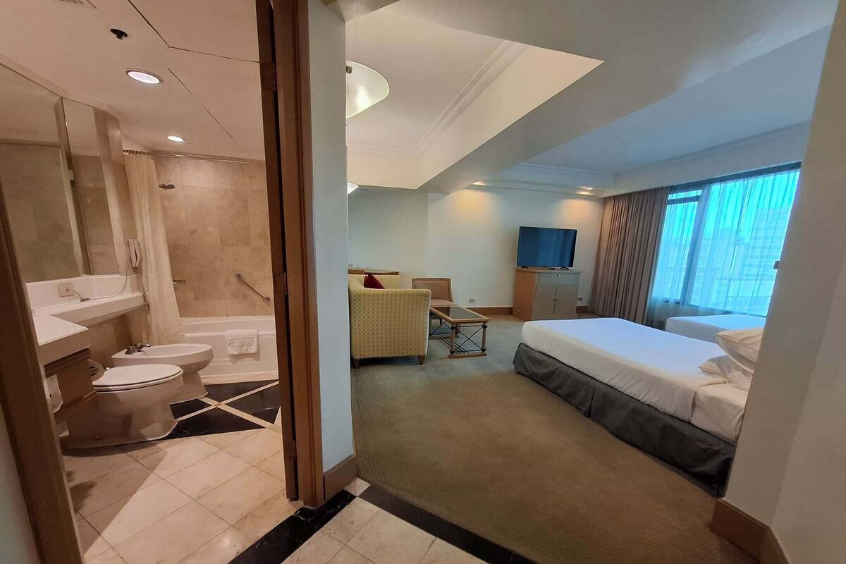 A hotel room with a bathroom, a bed, a desk, and a TV.