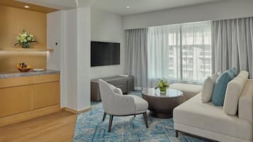 Una habitación de hotel moderna con sala de estar, cocina y un ventanal con cortinas.
